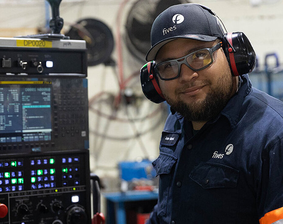 Machiniste portant des lunettes de sécurité et une protection auditive opérant un équipement d’usinage de précision dans une usine de fabrication.