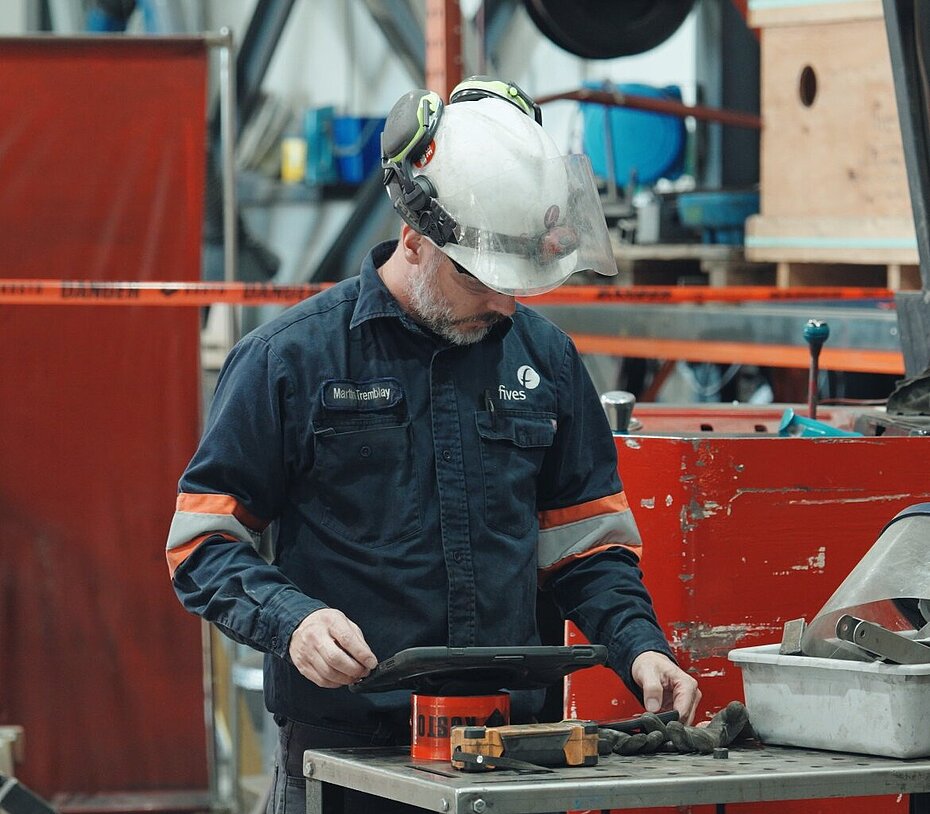 Employee wearing protective equipment and gloves operating tools at a workstation inside an industrial manufacturing facility.