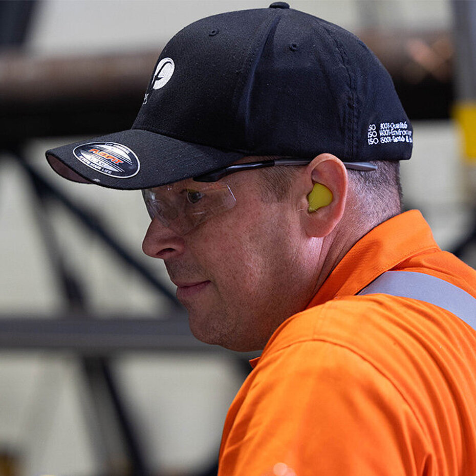 Employé portant des lunettes de sécurité, une protection auditive et des vêtements haute visibilité dans une installation industrielle.