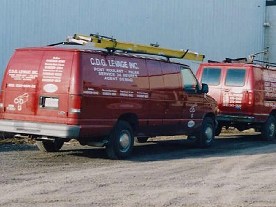 Camionnettes de service vintage stationnées à l’extérieur d’une installation industrielle, avec l’image de marque de l’entreprise et des équipements montés sur le toit.