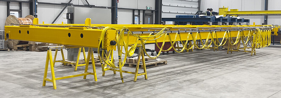 Poutres de pont roulant jaunes positionnées à l’intérieur d’une grande usine de fabrication industrielle avant leur installation ou leur assemblage.